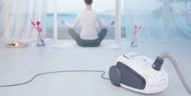 Një grua që bën joga me fshesën Ultra Silencer të Electrolux në sfond